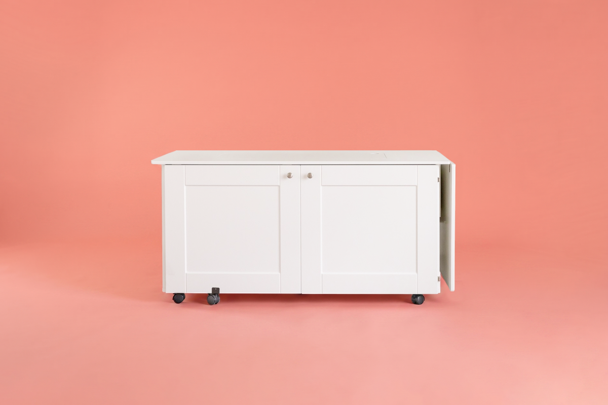 A white rolling storage cabinet with two paneled doors and black caster wheels, shown against a solid coral-pink background. [XL]