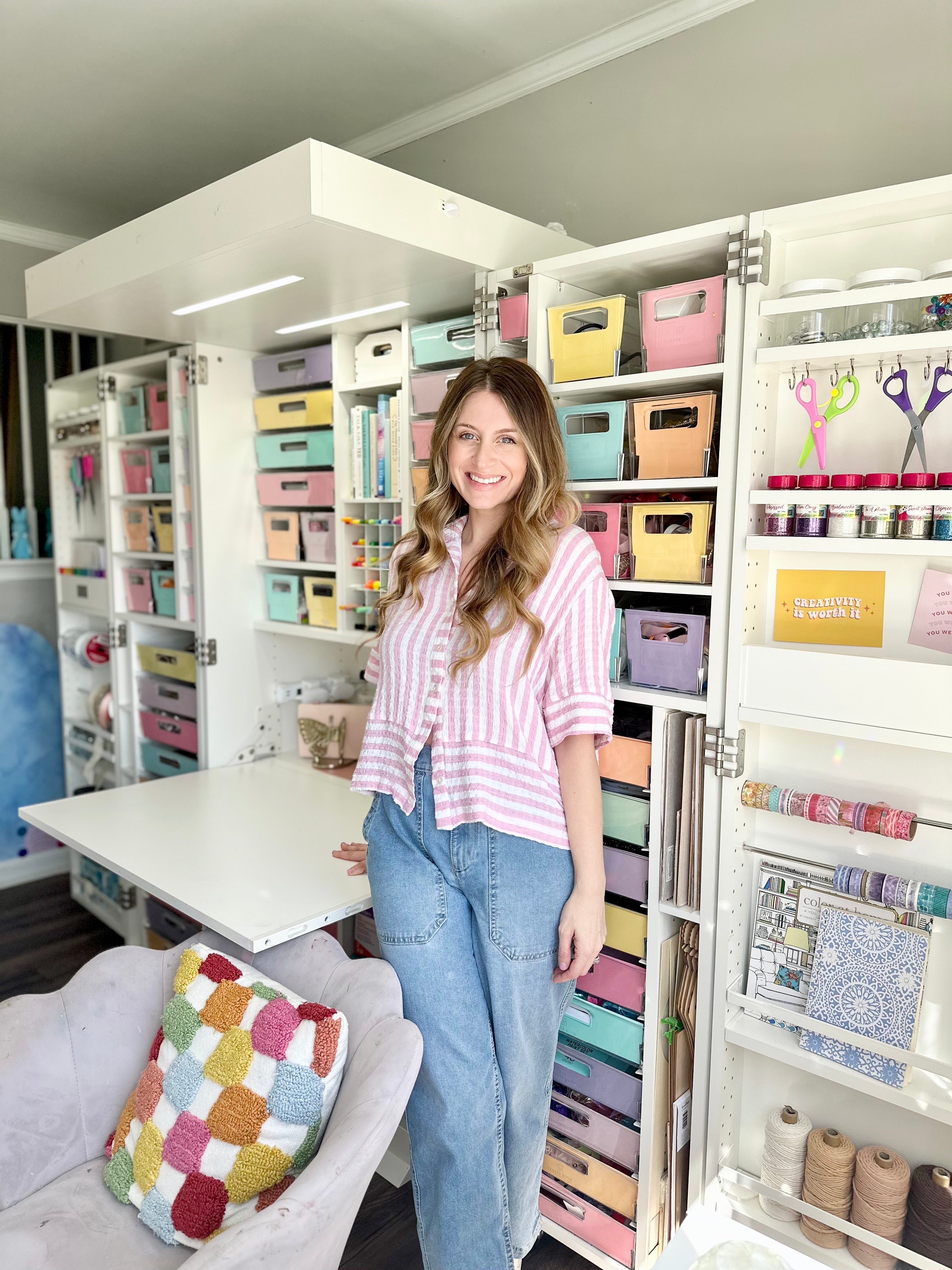 Woman standing in a craft room with shelves filled with craft supplies organized.