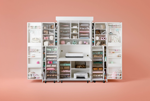 A white DreamBox storage system with various compartments and shelves, partially filled with items, set against a pink background.